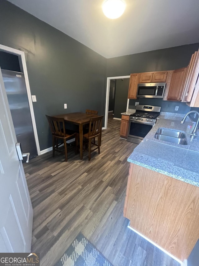 kitchen with light stone counters, dark wood finished floors, stainless steel appliances, a sink, and baseboards