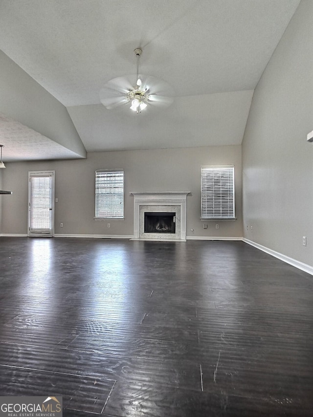 unfurnished living room with ceiling fan, a premium fireplace, vaulted ceiling, and dark wood-type flooring