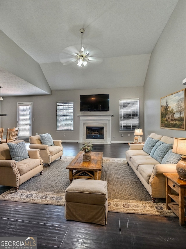 living area with vaulted ceiling, ceiling fan, dark wood-style flooring, and a glass covered fireplace