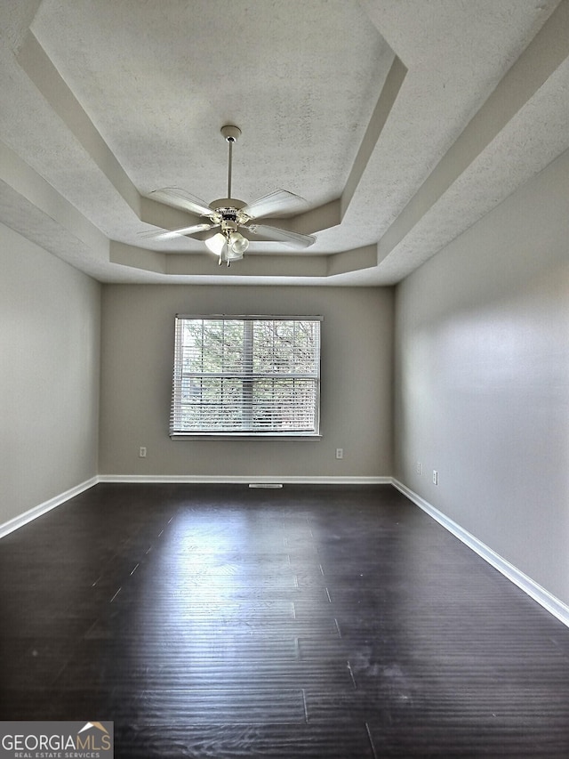 unfurnished room with ceiling fan, a textured ceiling, dark wood-type flooring, baseboards, and a raised ceiling