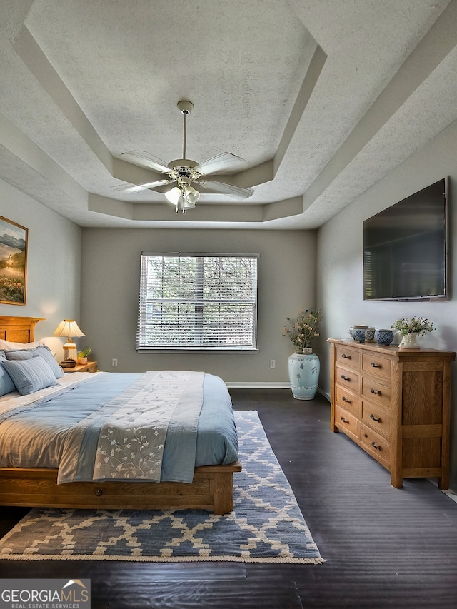 bedroom with dark wood-style floors, a tray ceiling, ceiling fan, a textured ceiling, and baseboards