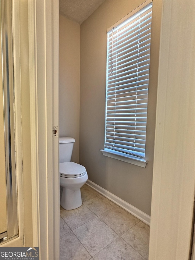 bathroom featuring a wealth of natural light, toilet, baseboards, and tile patterned floors