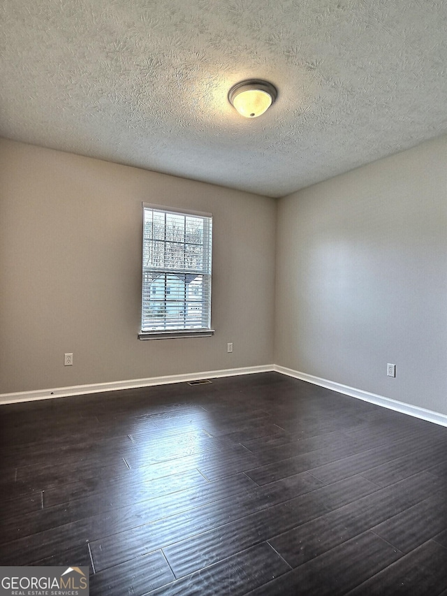 spare room with dark wood-style floors, a textured ceiling, and baseboards