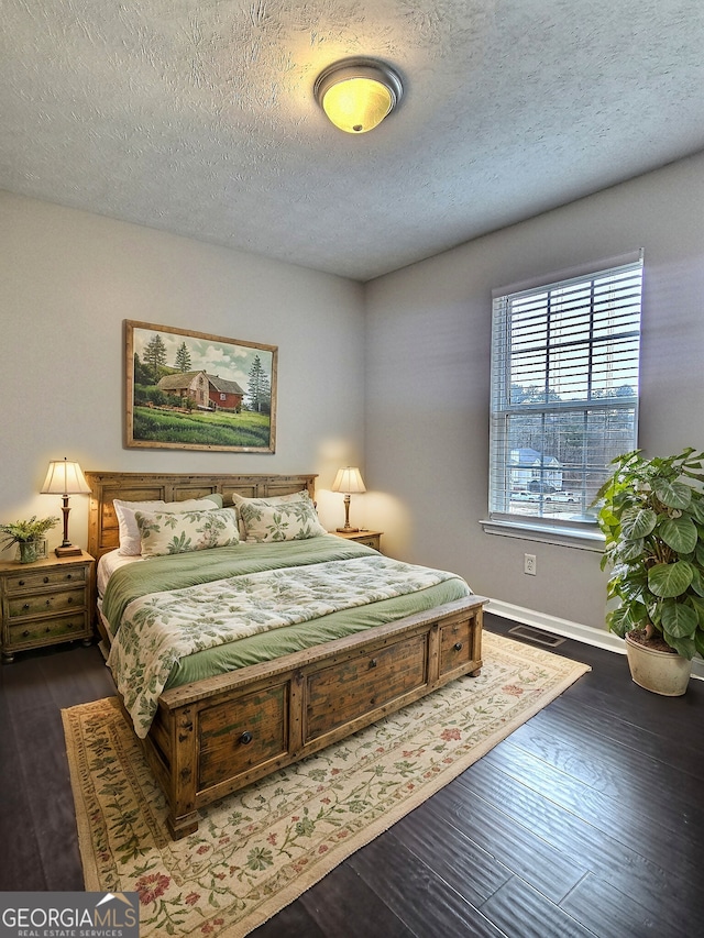 bedroom with a textured ceiling, dark wood finished floors, visible vents, and baseboards