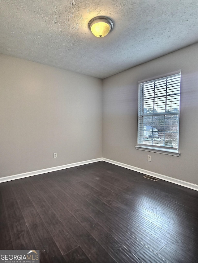 unfurnished room featuring visible vents, baseboards, dark wood finished floors, and a textured ceiling