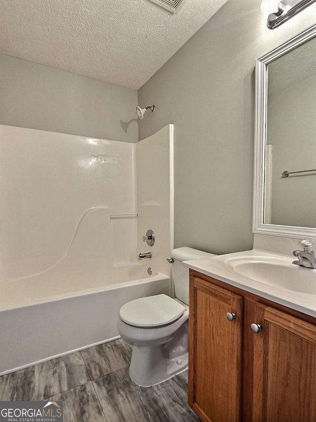 bathroom featuring a textured ceiling,  shower combination, toilet, and vanity