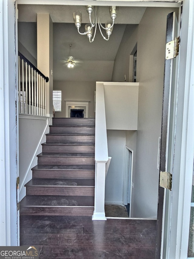 stairway featuring wood finished floors and ceiling fan with notable chandelier