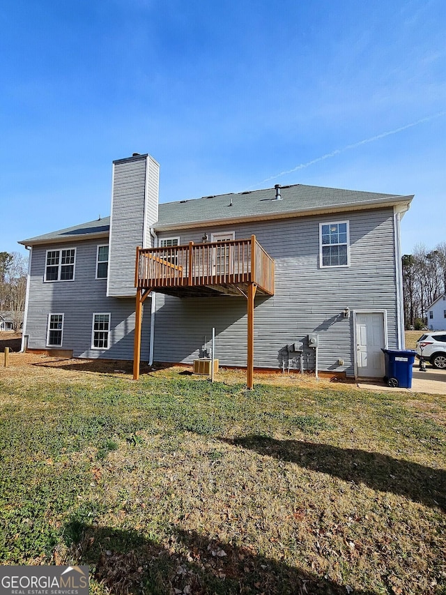 rear view of property featuring a chimney, a yard, and a deck