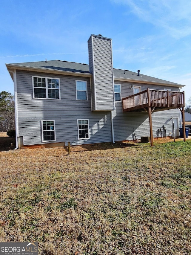 rear view of property featuring a yard, a chimney, a wooden deck, and central air condition unit