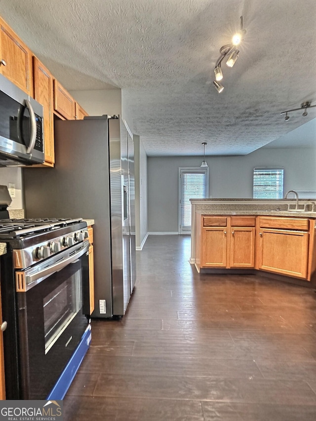 kitchen featuring baseboards, dark wood-style floors, decorative light fixtures, stainless steel appliances, and a sink