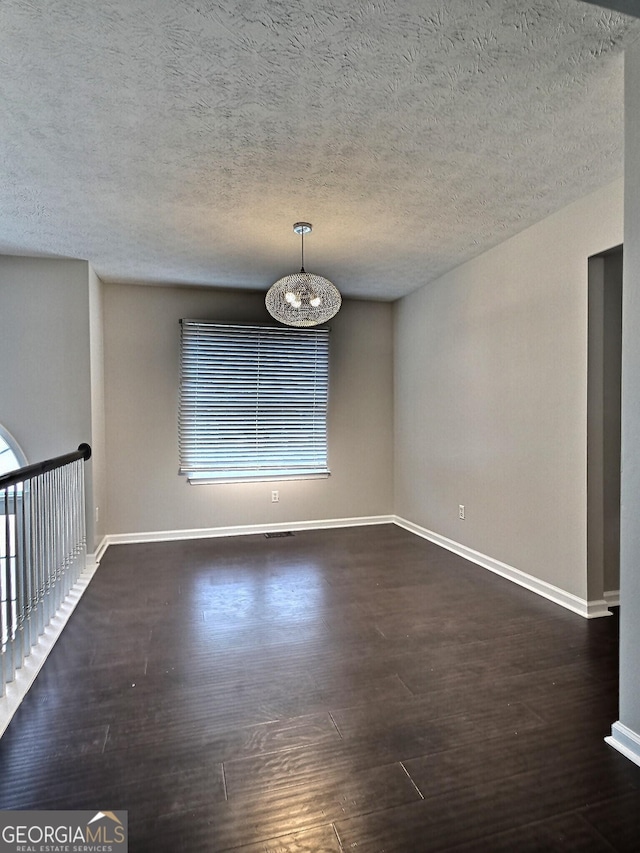 spare room featuring a notable chandelier, dark wood-style flooring, and baseboards