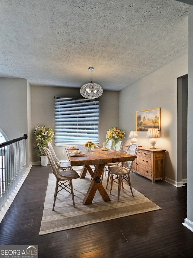 dining space featuring dark wood-style floors, a textured ceiling, baseboards, and a notable chandelier