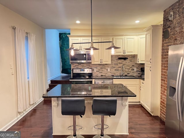 kitchen with dark wood-style flooring, a sink, appliances with stainless steel finishes, decorative backsplash, and dark stone counters