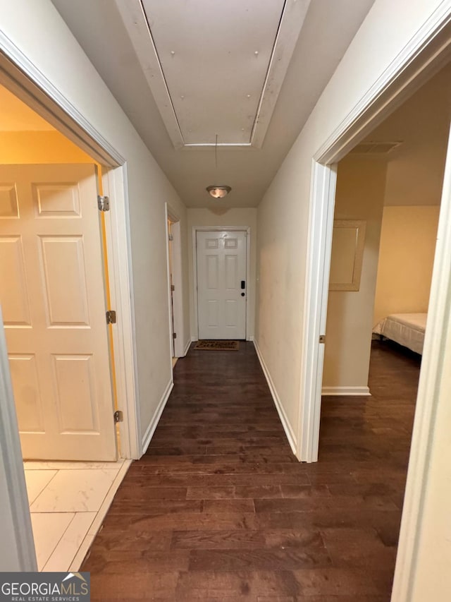 hallway featuring dark wood-style floors, attic access, and baseboards