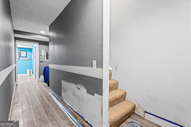 hallway featuring a textured ceiling, light wood finished floors, and stairs