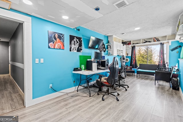 office space with baseboards, visible vents, a textured ceiling, and light wood finished floors