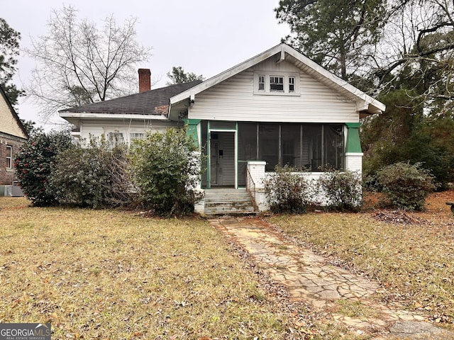 view of front of house with a sunroom, a chimney, and a front yard