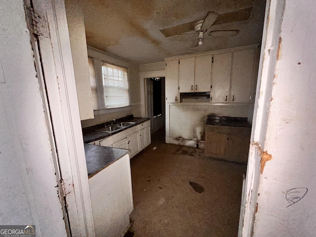 kitchen featuring dark countertops, white cabinetry, a sink, and ceiling fan