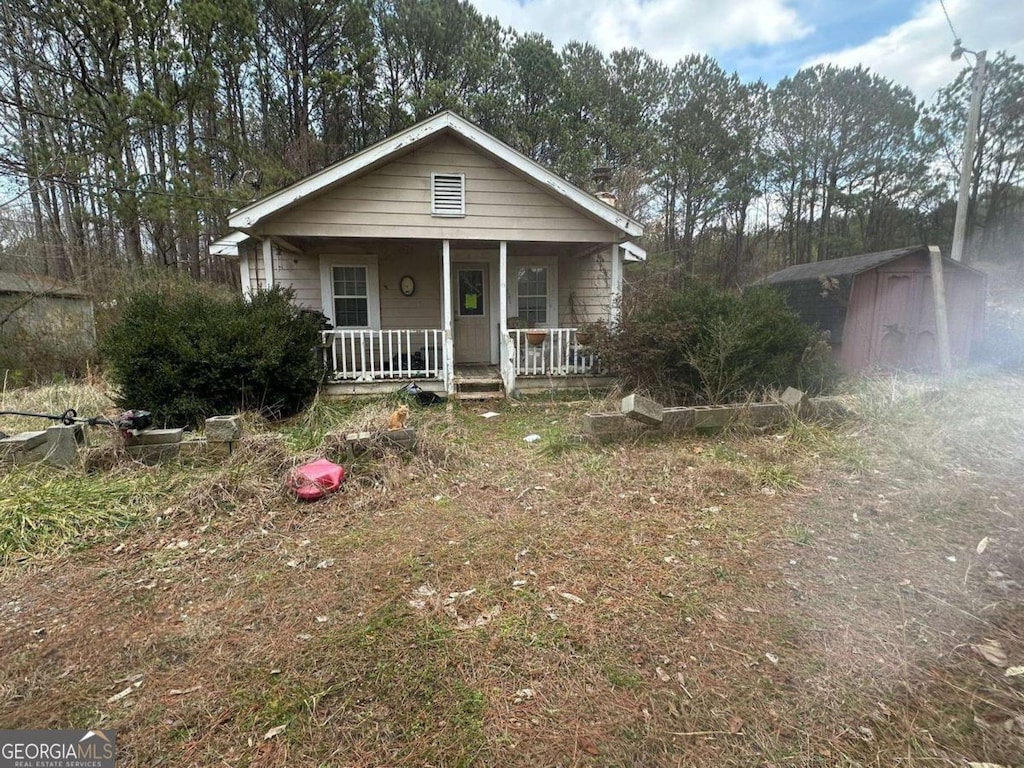 bungalow-style home with covered porch, a storage unit, and an outbuilding