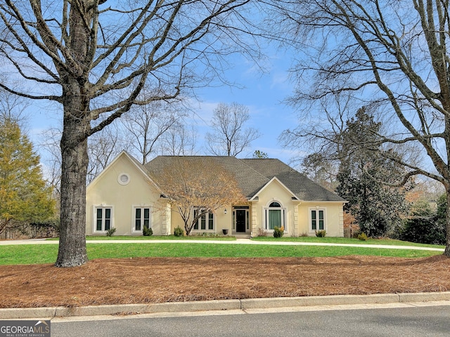 view of front facade featuring stucco siding, roof with shingles, and a front yard