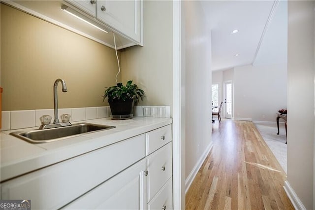 bar featuring light wood-style flooring, baseboards, a sink, and recessed lighting