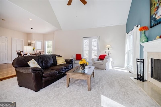 living room with plenty of natural light, a premium fireplace, high vaulted ceiling, and ceiling fan with notable chandelier