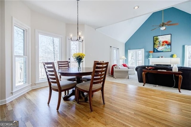 dining space with a healthy amount of sunlight, light wood-style floors, a fireplace, and high vaulted ceiling