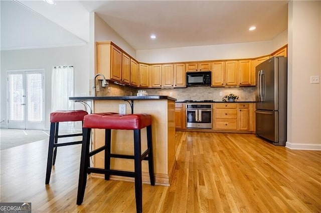 kitchen with light wood finished floors, decorative backsplash, dark countertops, appliances with stainless steel finishes, and a peninsula