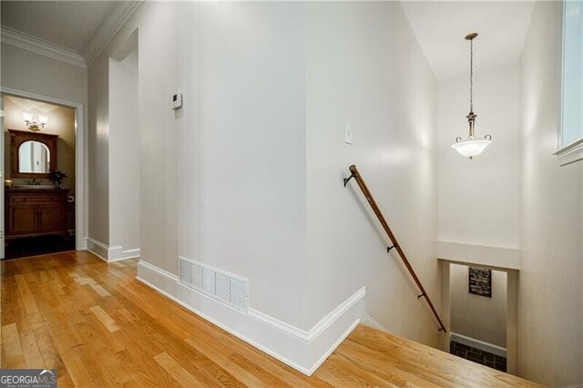 corridor featuring light wood-type flooring, visible vents, baseboards, and an upstairs landing