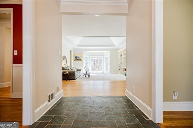 hallway featuring visible vents, baseboards, dark wood-style floors, a raised ceiling, and crown molding