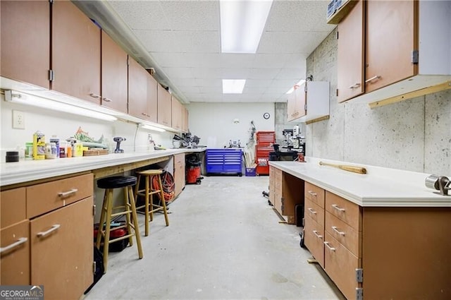 kitchen with concrete flooring, light countertops, a drop ceiling, and a kitchen breakfast bar