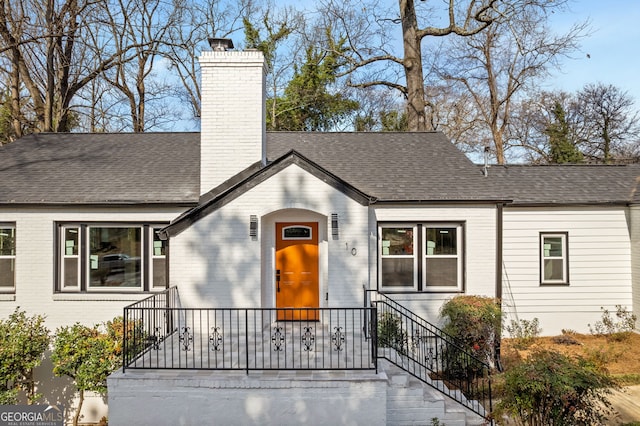 view of front of home featuring a shingled roof, brick siding, and a chimney