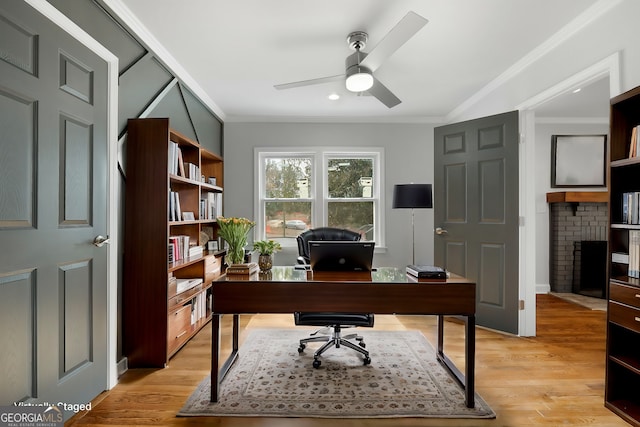 office area featuring light wood-style floors, a fireplace, a ceiling fan, and crown molding