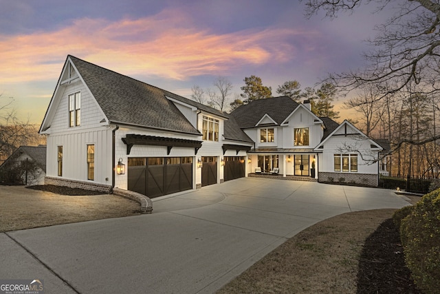 modern inspired farmhouse featuring a garage, driveway, roof with shingles, board and batten siding, and a chimney