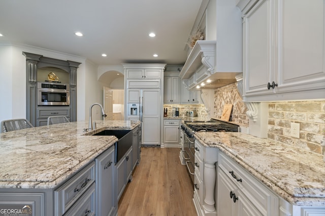 kitchen with arched walkways, decorative backsplash, high end appliances, wall chimney range hood, and a sink