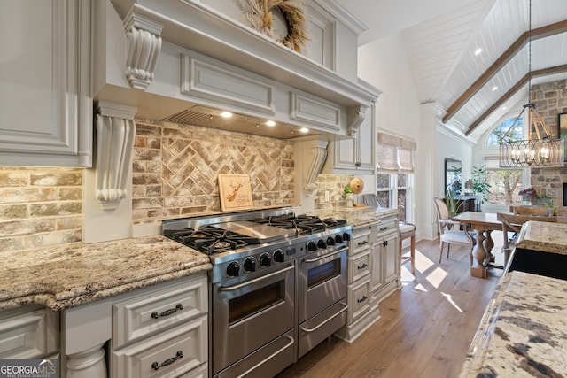 kitchen featuring light stone counters, wood finished floors, backsplash, double oven range, and an inviting chandelier