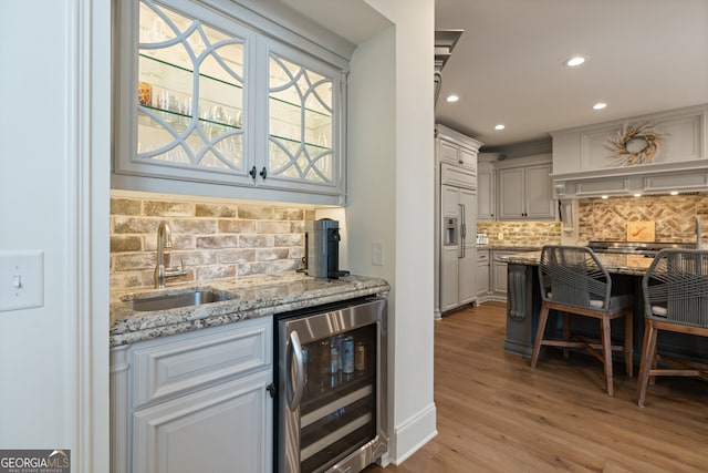 kitchen featuring light stone counters, wine cooler, light wood finished floors, a sink, and paneled fridge