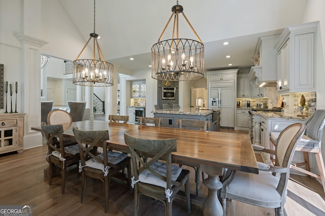 dining room with a chandelier, high vaulted ceiling, wine cooler, recessed lighting, and wood finished floors