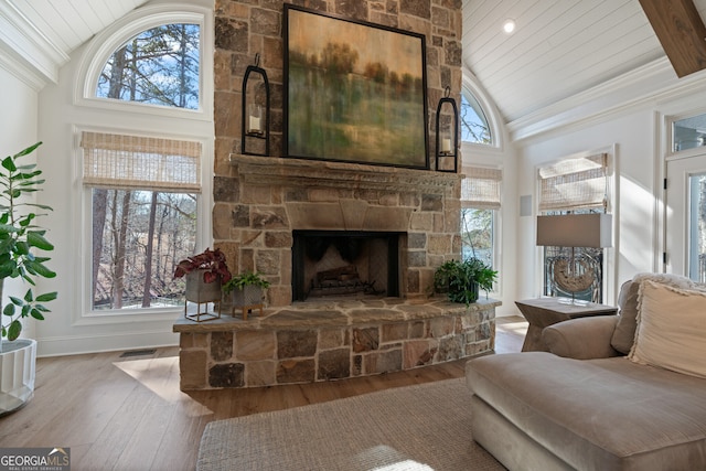 living room with a wealth of natural light, visible vents, wood finished floors, and a stone fireplace