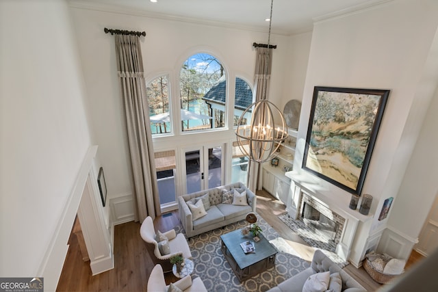 living area with a wainscoted wall, wood finished floors, an inviting chandelier, crown molding, and a decorative wall