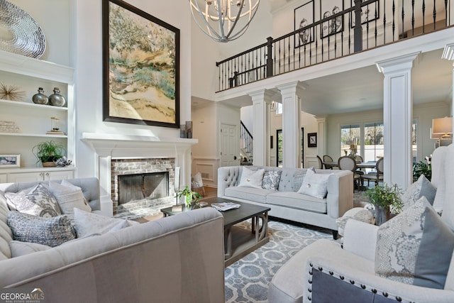 living room with crown molding, built in shelves, a brick fireplace, and ornate columns