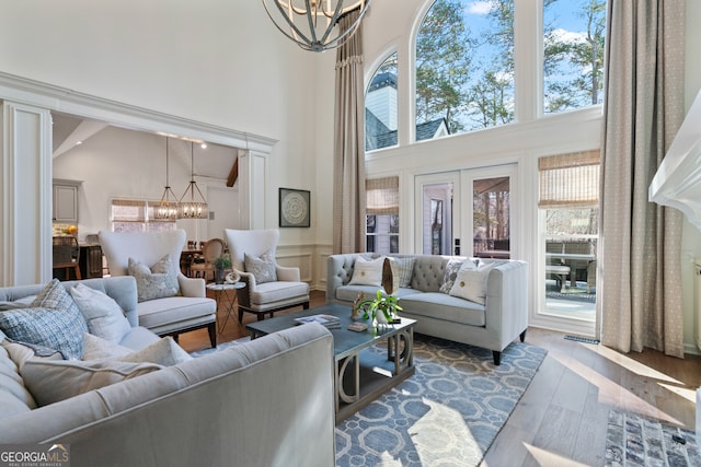 living area with french doors, a decorative wall, a towering ceiling, an inviting chandelier, and wood finished floors