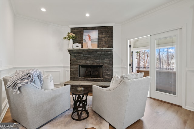 living area featuring a wainscoted wall, a fireplace, crown molding, a decorative wall, and wood finished floors