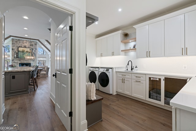 clothes washing area featuring arched walkways, dark wood-style flooring, a sink, and washing machine and clothes dryer