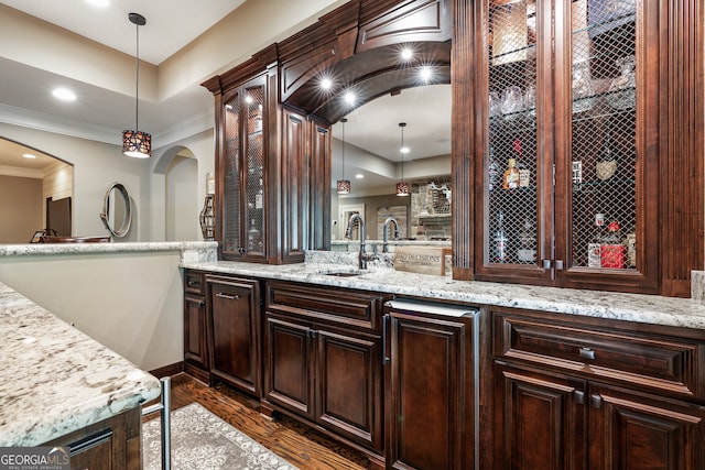 bar with arched walkways, dark wood finished floors, ornamental molding, hanging light fixtures, and a sink