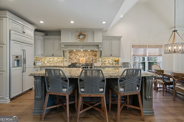 kitchen featuring tasteful backsplash, wood finished floors, light stone countertops, a kitchen island with sink, and paneled fridge