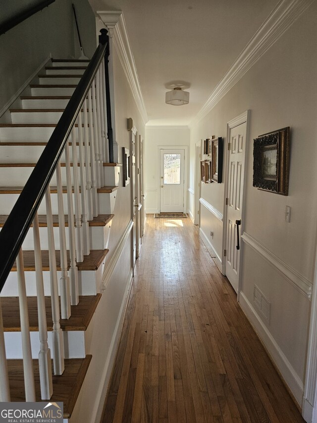 hallway with visible vents, dark wood-type flooring, ornamental molding, baseboards, and stairs