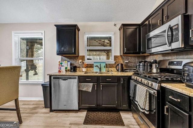 kitchen with light stone counters, a sink, stainless steel appliances, light wood-type flooring, and backsplash