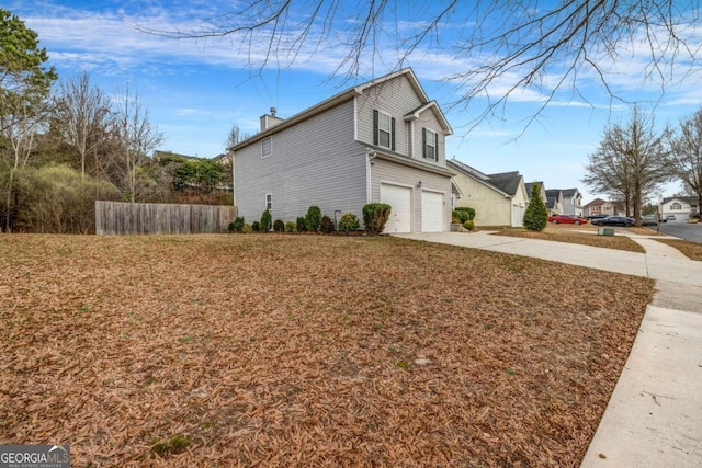 view of side of home featuring driveway, a chimney, an attached garage, and fence