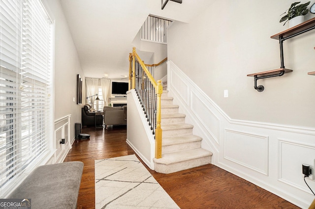 stairway with wainscoting, a fireplace, a decorative wall, and wood finished floors